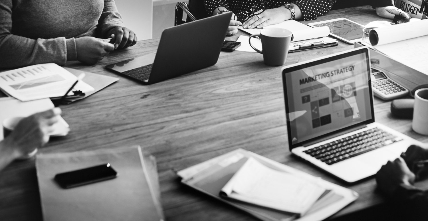 Réunion de stratégie marketing avec ordinateurs portables, documents et tasses de café sur une table en bois, illustrant l'intégration des outils numériques pour optimiser les performances commerciales.